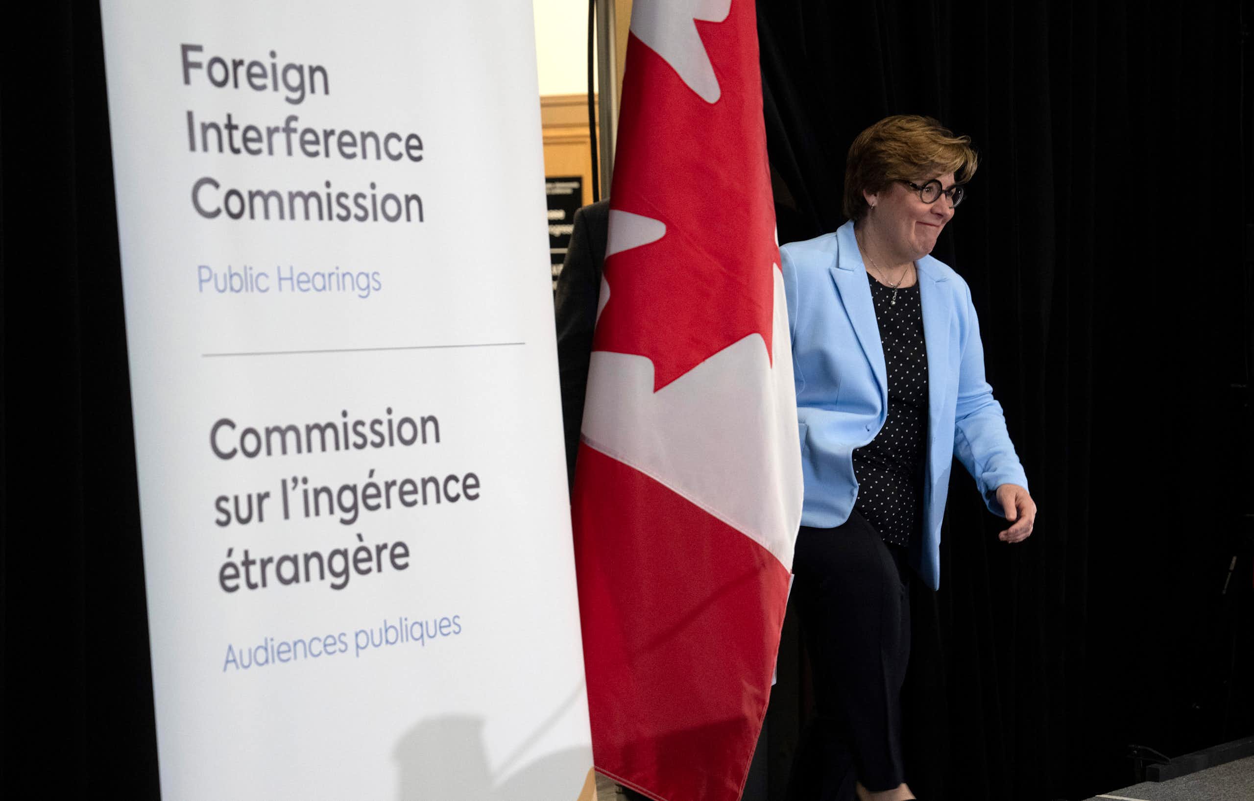 A woman in a pale blue jacket and wearing glasses appears next to a banner that read Foreign Interference Commission.