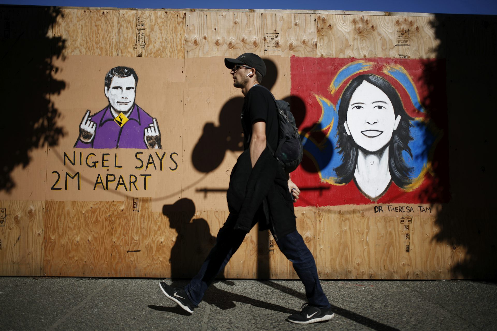 A man walks past a mural of a man and a woman with text reading: Nigel says 2 metres apart