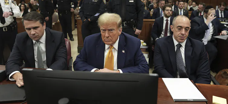 A man with blond/white hair glowers while sitting in a courtroom.