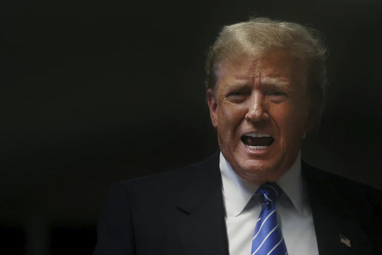 A man with blond/white hair grimaces as he speaks.