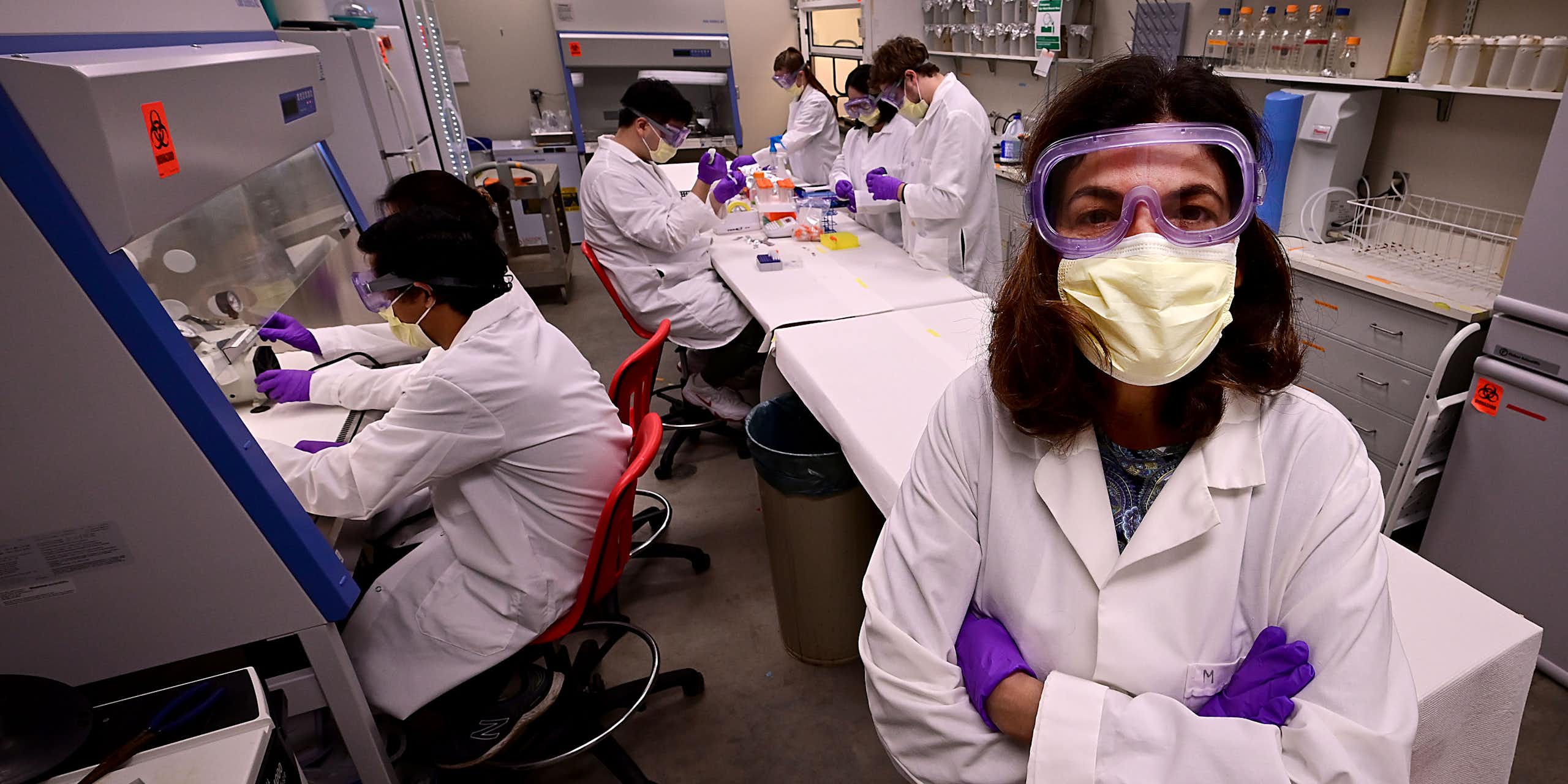 woman with arms crossed in lab setting with many workers in PPE