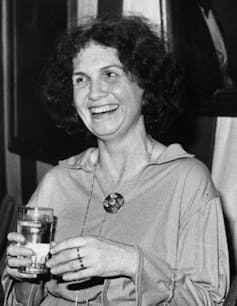 A woman smiling in profile holding a glass with rings seen on her fingers.
