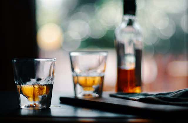 Two glasses half-filled with amber liquid sit next to a bottle of whiskey on a table.