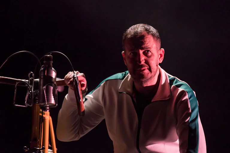 An actor crouches next to a bike