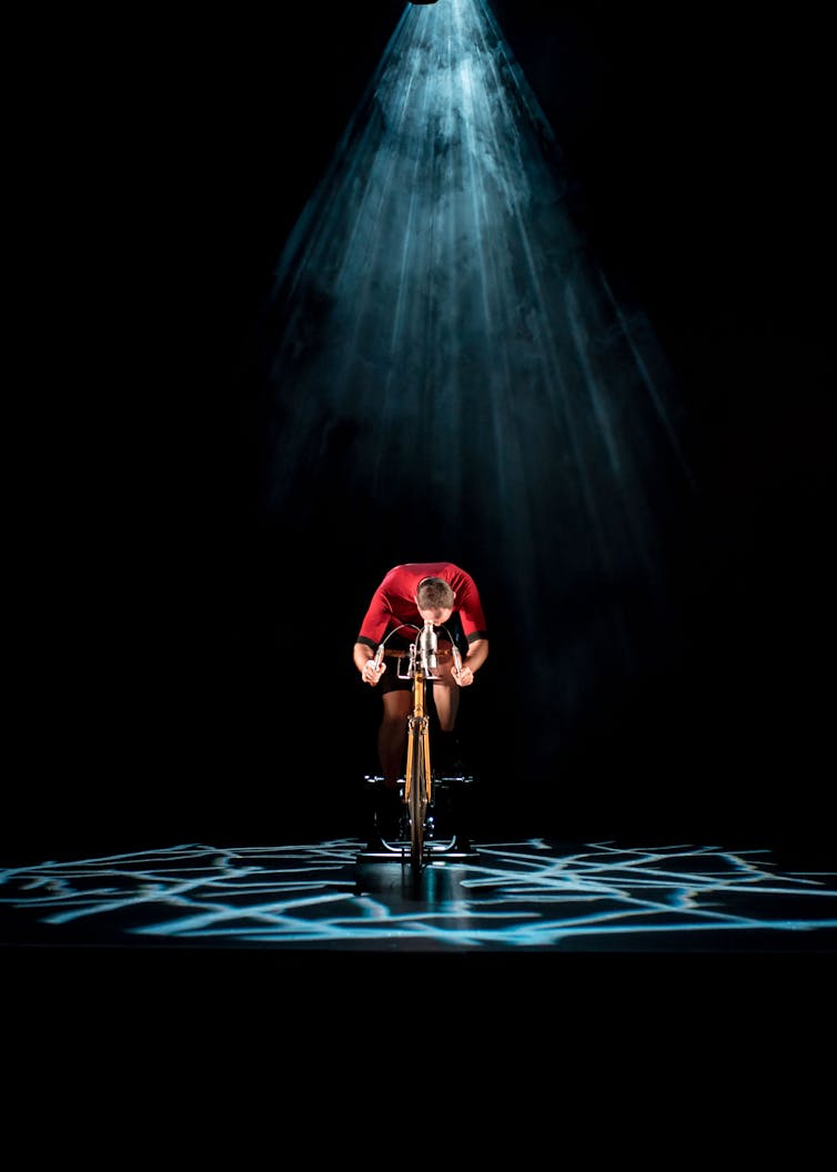 A man cycles under a spotlight.