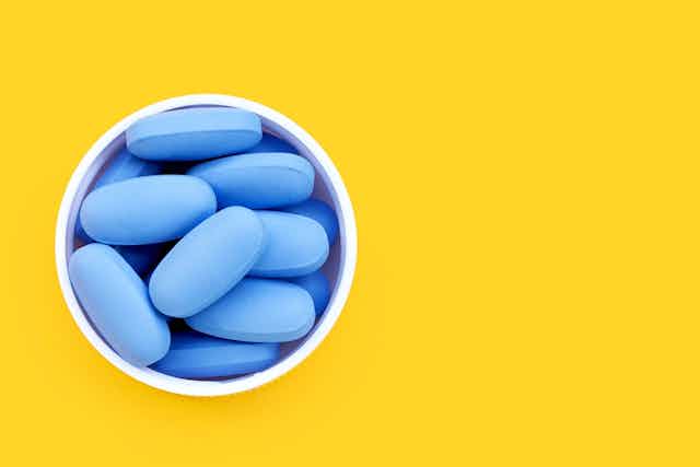 Top view of blue pills in white cup against yellow background