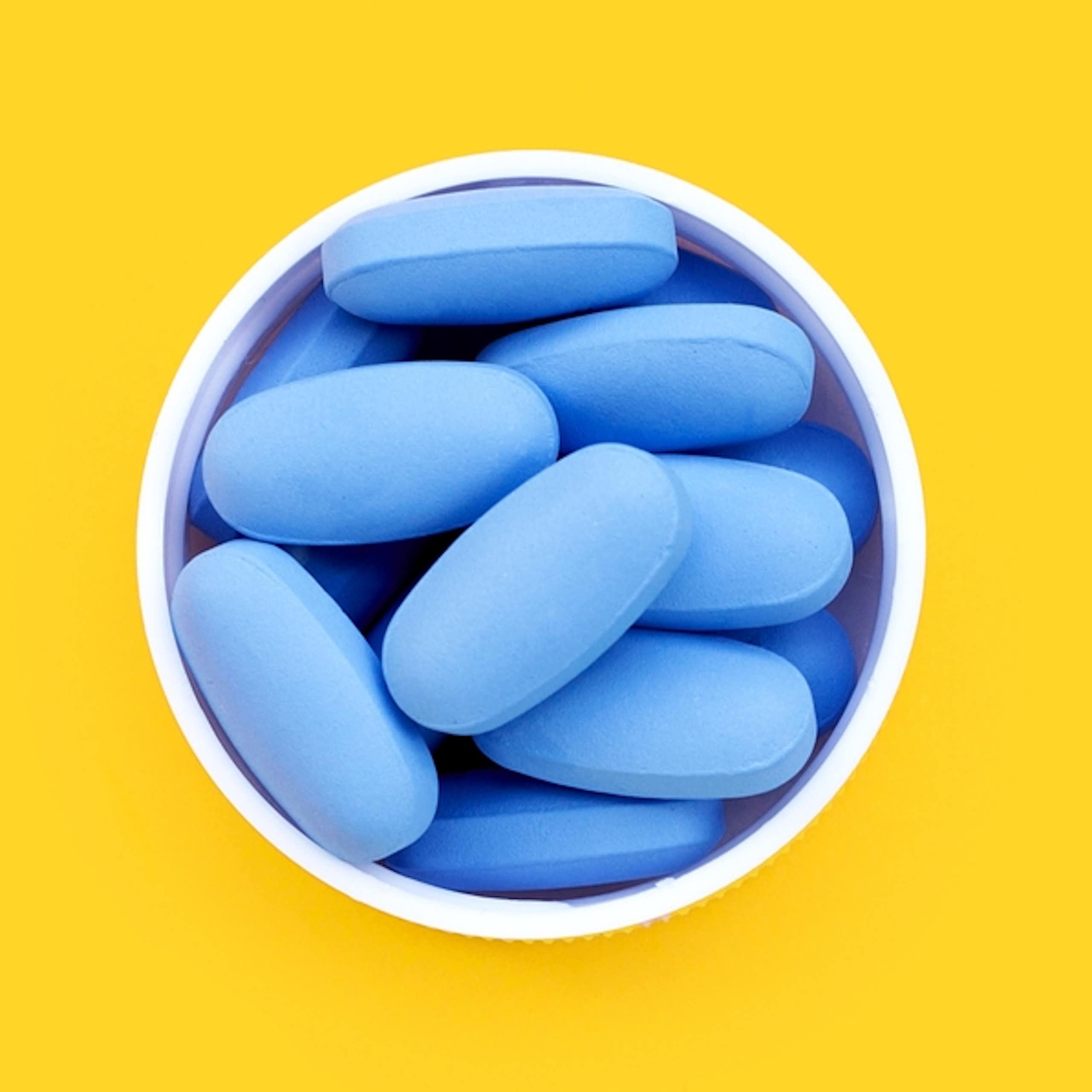 Top view of blue pills in white cup against yellow background
