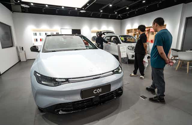 People inside a car showroom looking at two electric vehicles.