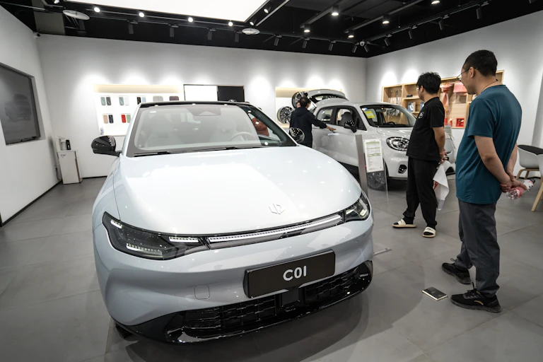 People inside a car showroom looking at two electric vehicles.