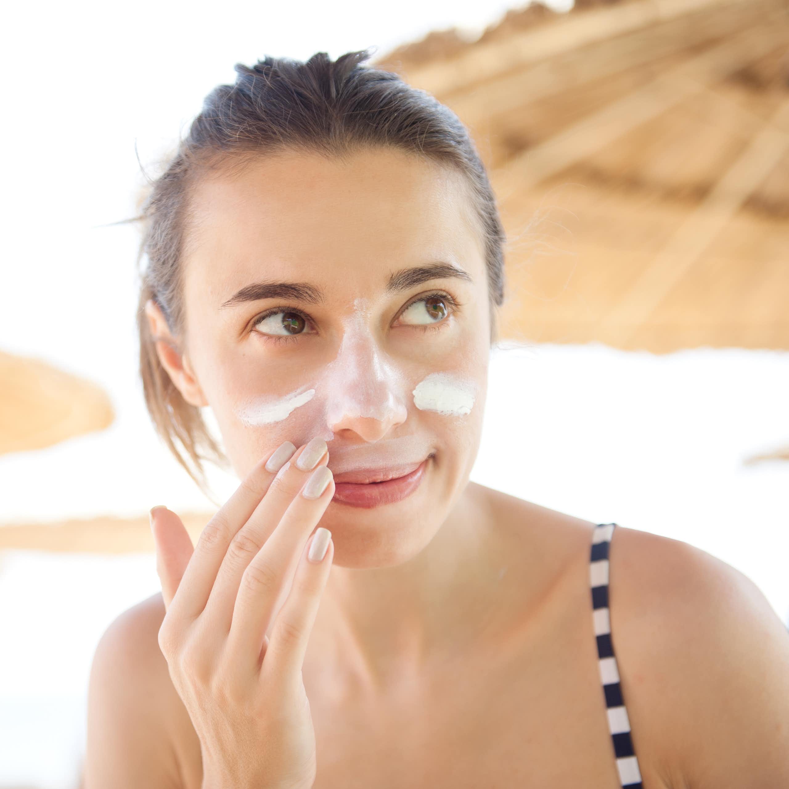A woman applies sunscreen to her face.