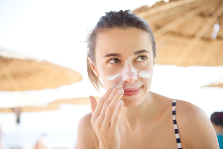 A woman applies sunscreen to her face.