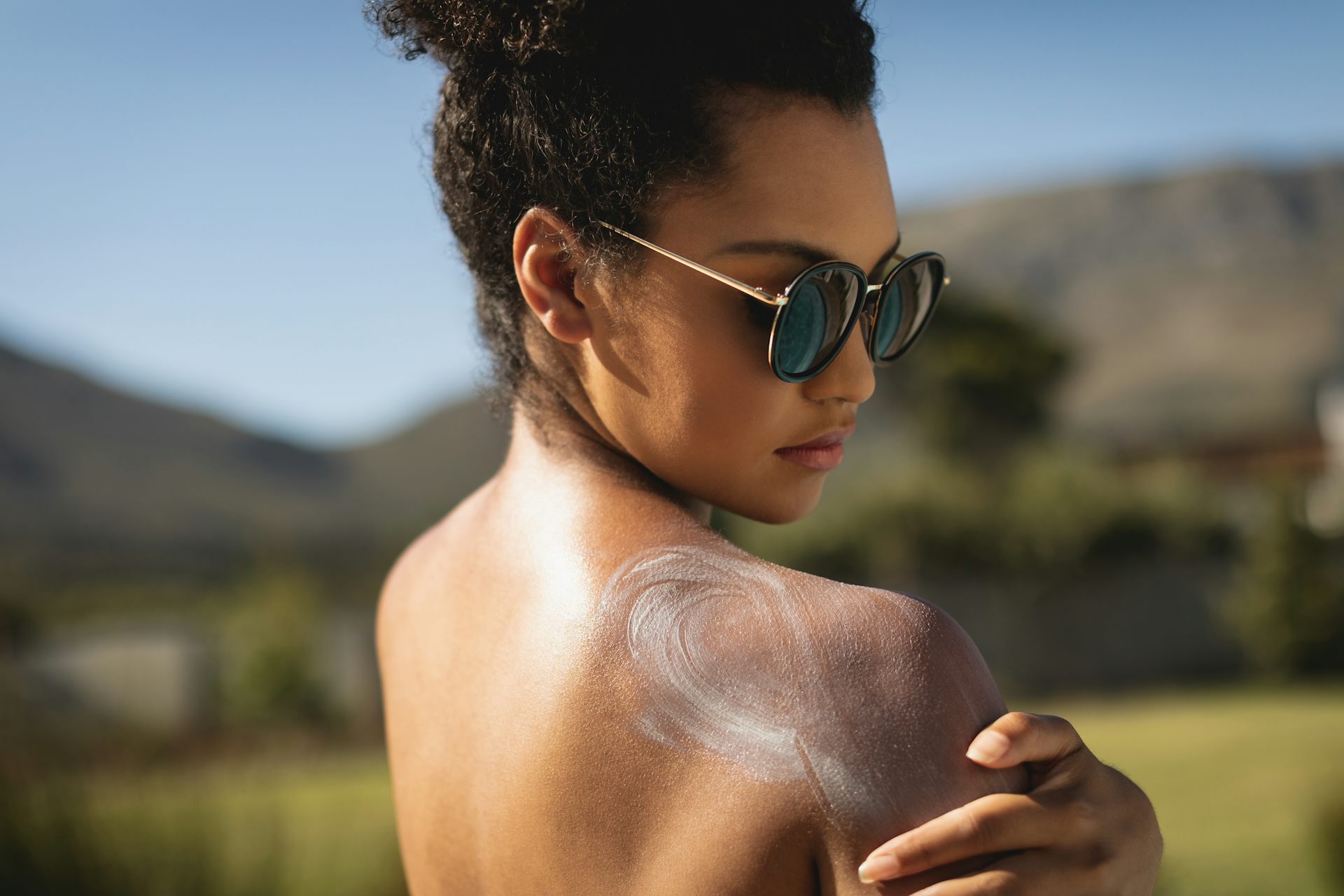 A woman is applying sunscreen to her shoulders.
