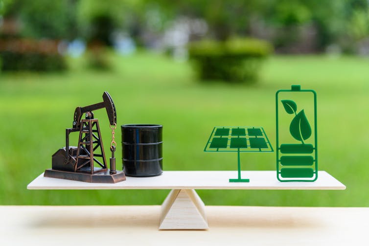 weighing scales concept with fossil fuels on left and green energy on right, blurry green garden background