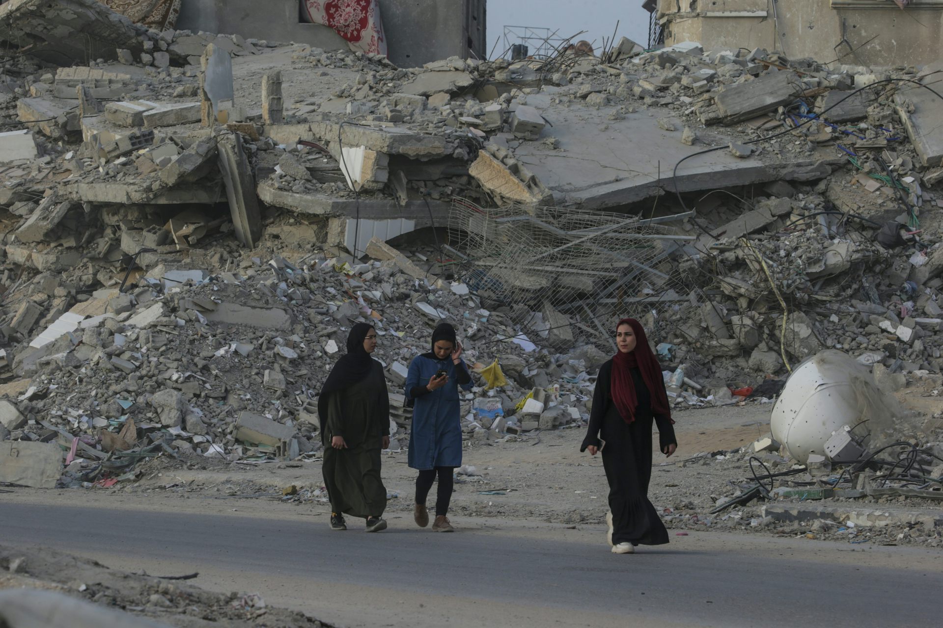 Three women walking down a road against the backdrop of a war-damaged city.