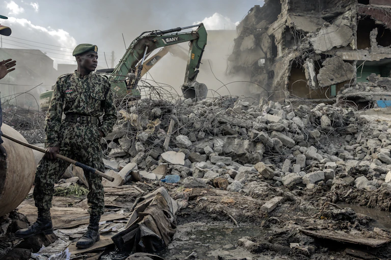 Man in military fatigue stands in front of rubble.