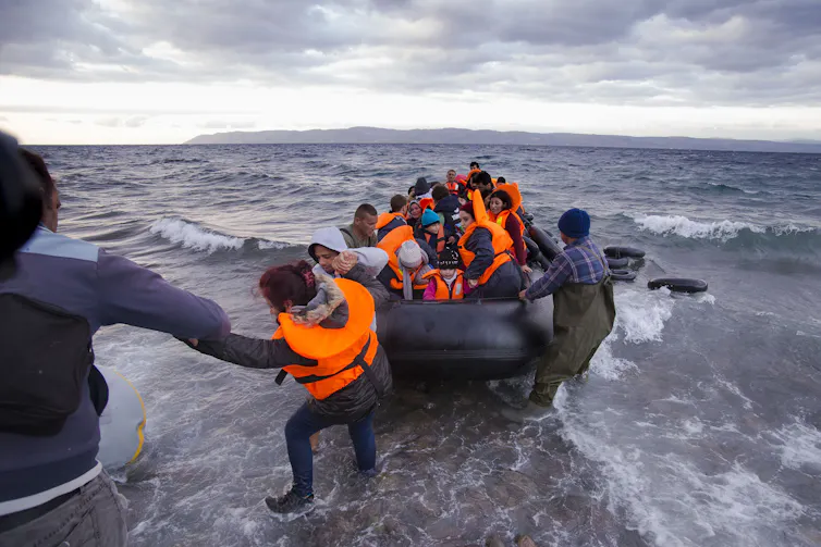 Refugees are helped out of a small rubber dinghy as they reach the island of Lesvos in Greece