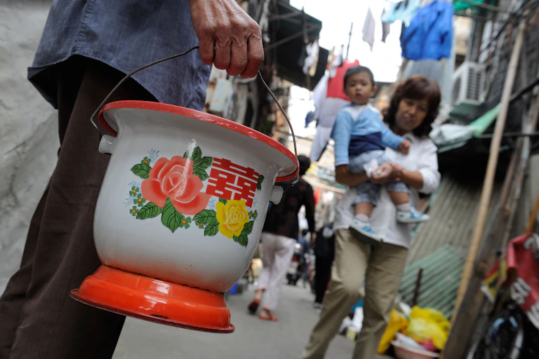 A man carries a decorative chamber pot in an alley.