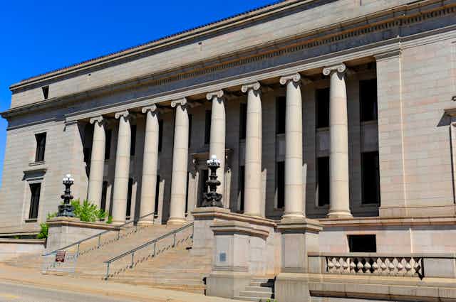 A large granite building with columns and a big staircase in front.