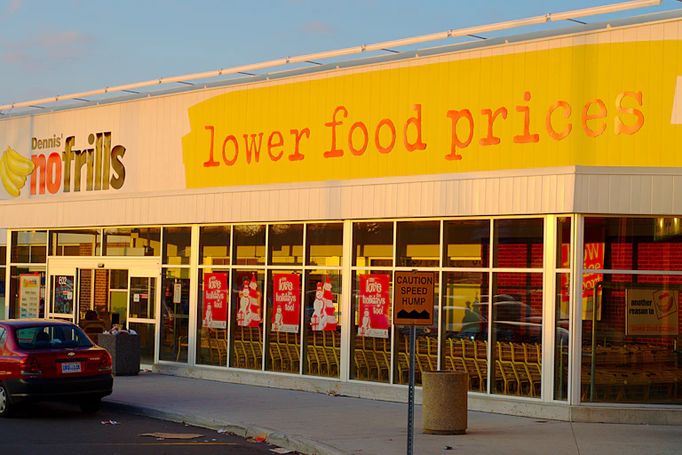 Storefront of a Canadian grocer, with "lower food prices" painted largely on the facade
