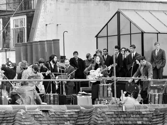 A black and white photo of The Beatles playing on the roof of a building.