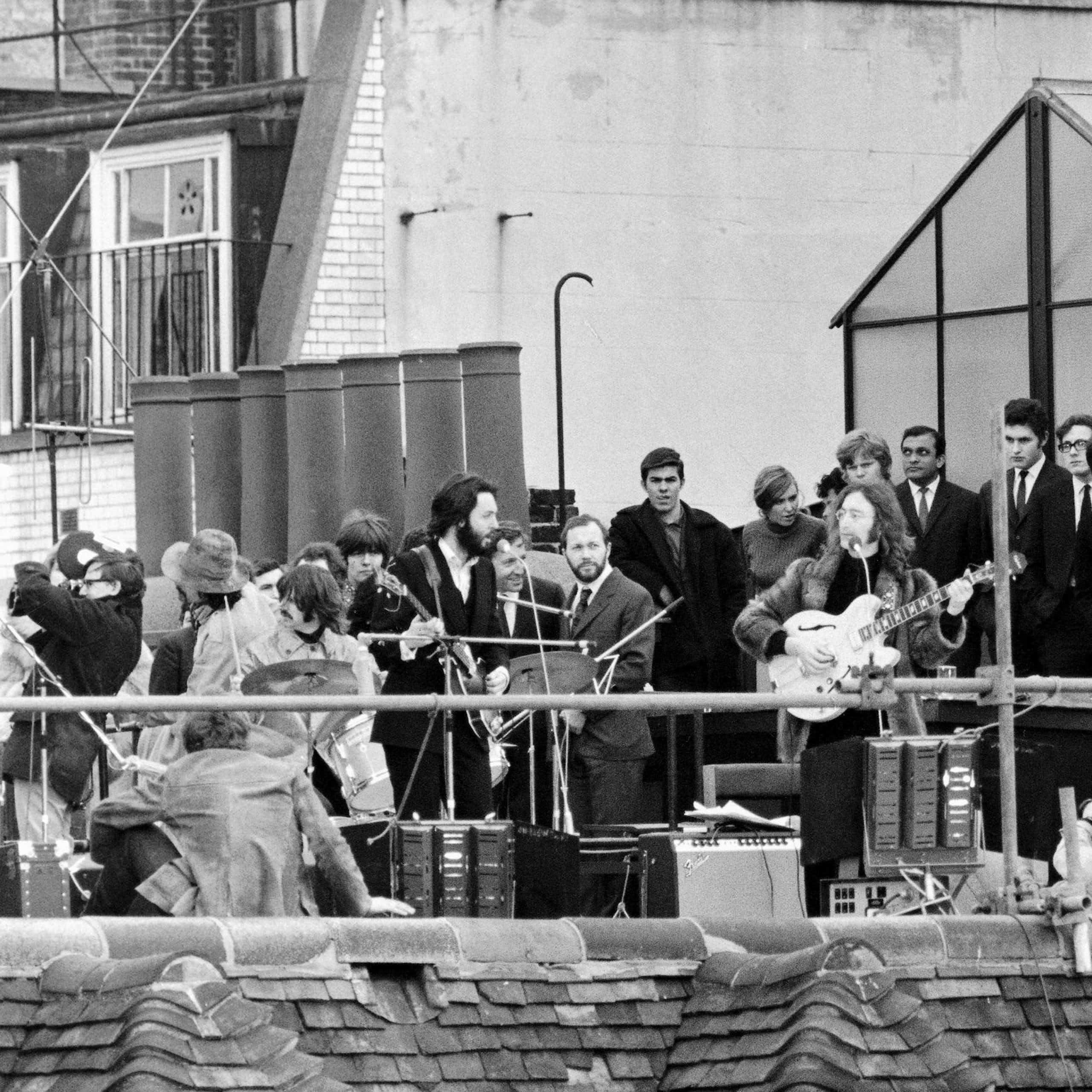 A black and white photo of The Beatles playing on the roof of a building.
