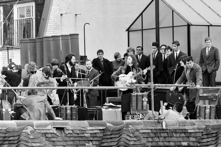 A black and white photo of The Beatles playing on the roof of a building.