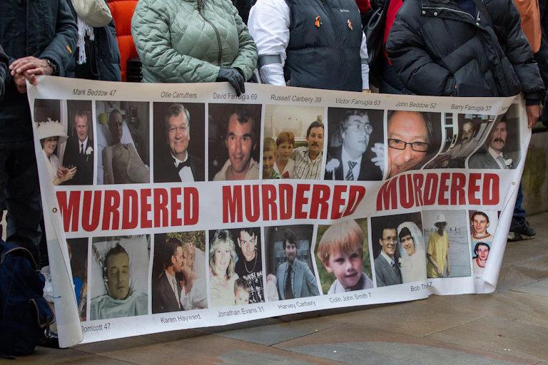 People holding up a banner showing the faces of their family members who have died
