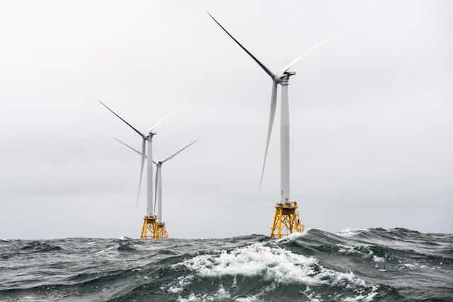 Three offshore wind turbines in turbulent water.