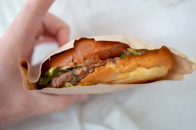 A burger on a bread patty, covered with a brown paper bag, is seen in a person's hand.