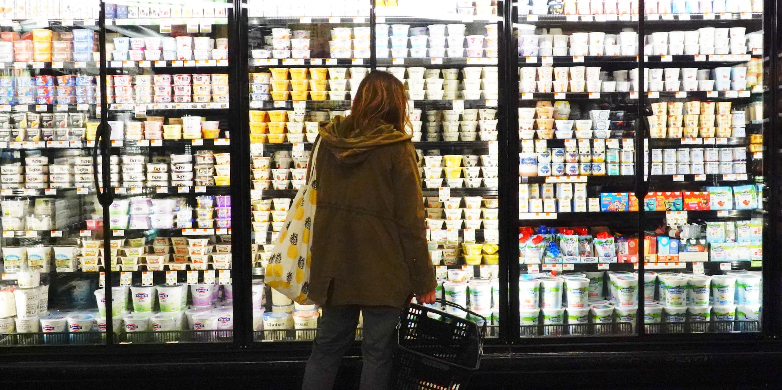 A person is seen from behind examining freezers full of dairy products at a Brooklyn grocery store.