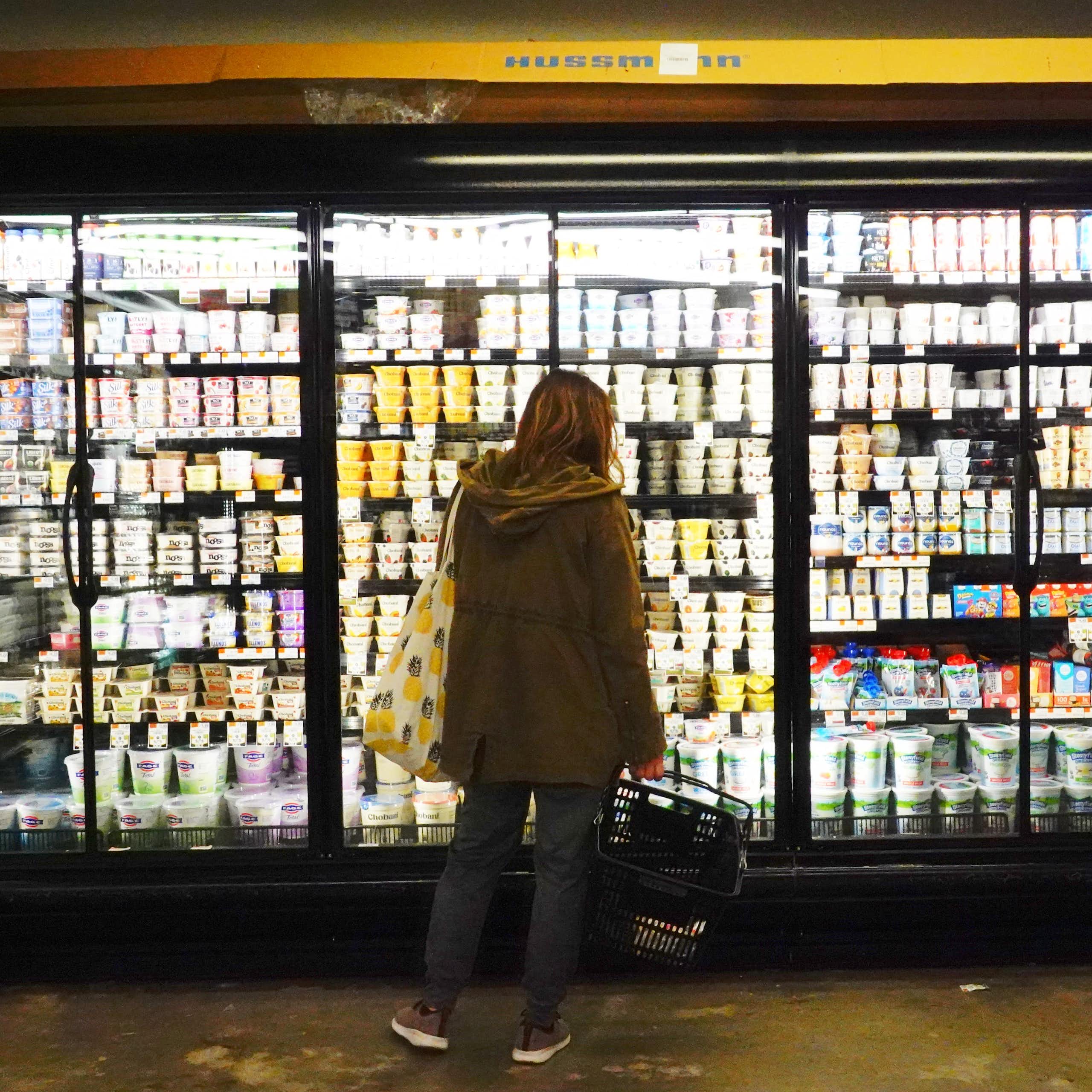 A person is seen from behind examining freezers full of dairy products at a Brooklyn grocery store.
