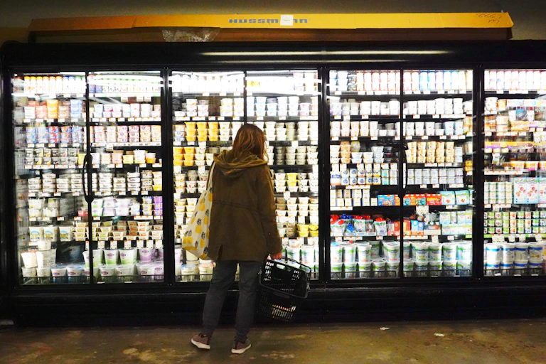 A person is seen from behind examining freezers full of dairy products at a Brooklyn grocery store.