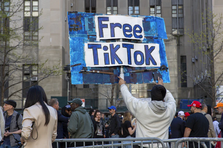 A person holds a handmade sign at the edge of a crowd outdoors in front of a large building