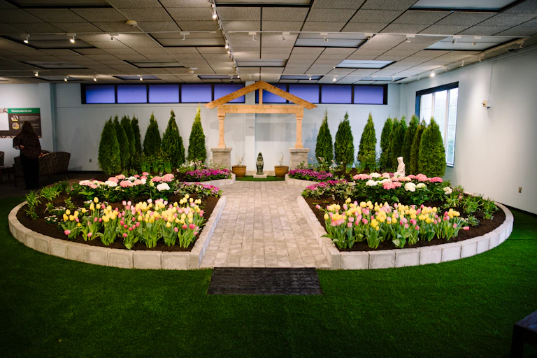 A garden with colorful flowers and plants surrounding a statue of the Virgin Mary.