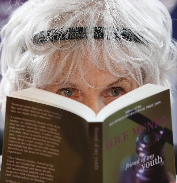 A woman holds a book near her face partly obscuring herself.