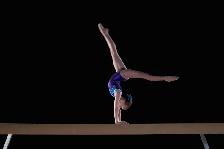 Young girl performing a handstand on balance beam in a leotard
