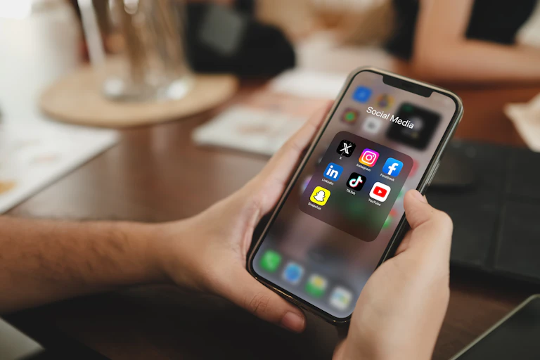 A man holds an iPhone with a folder of social media apps on the screen, including Facebook and Instagram