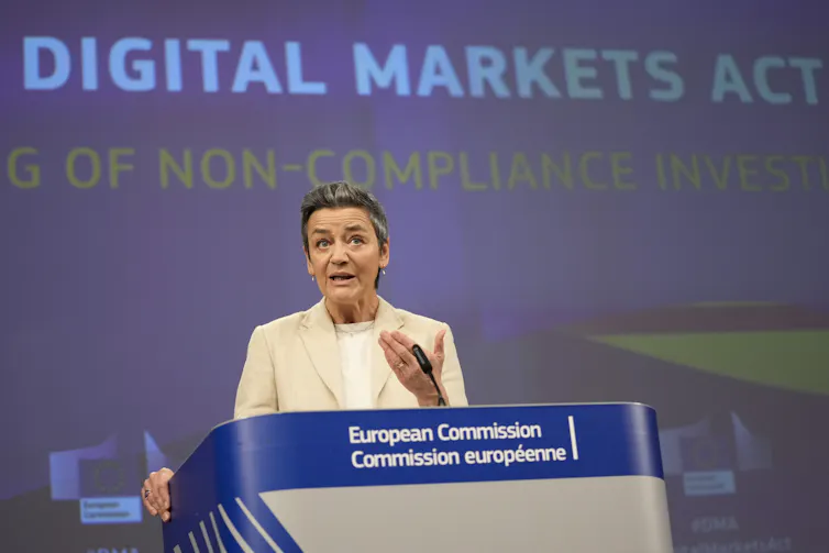 A woman stands in front of a large screen saying Digital Markets Act and speaks at a lectern