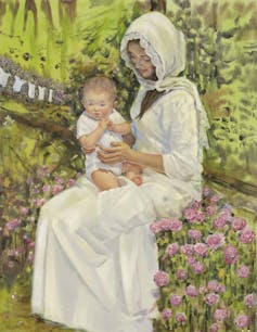 A woman dressed in a white garment holding a baby on her lap while sitting amid pink flowers with baby clothes hanging on a lavender bush in the background.