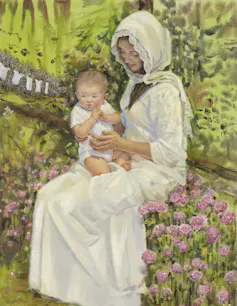 A woman dressed in a white garment holding a baby on her lap while sitting amid pink flowers with baby clothes hanging on a lavender bush in the background.