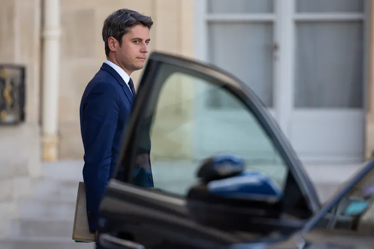 A young man in a suit walks past an open car door