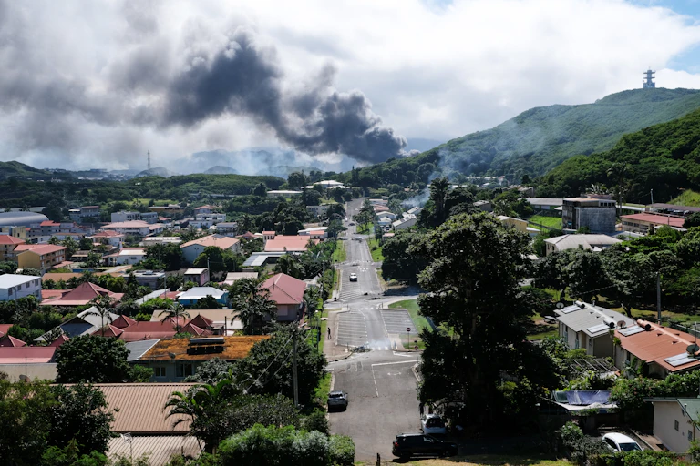 A drone view of a tropical township with plumes of smoke in the distance