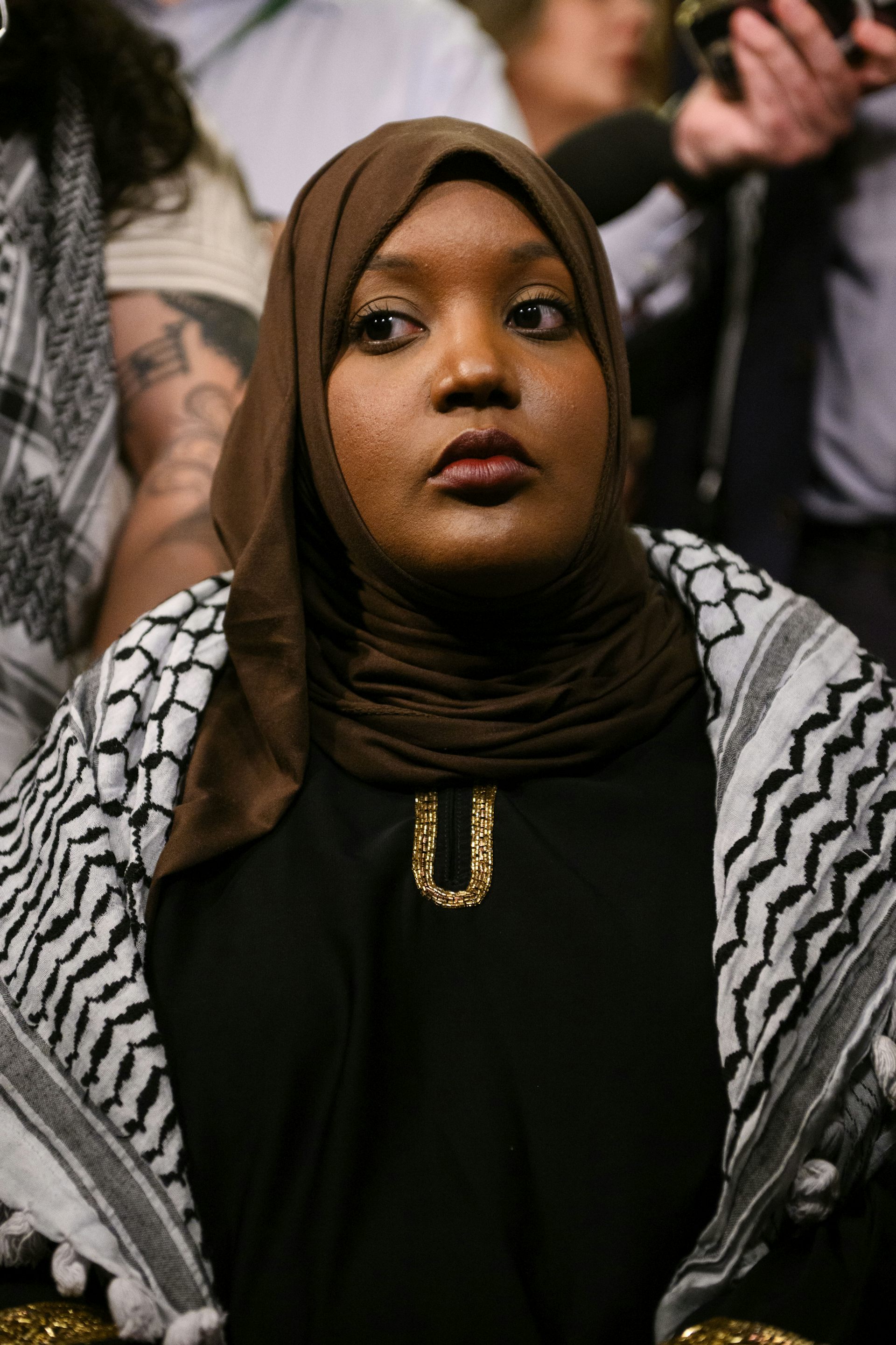 A Black woman wearing a hijab and a keffiyeh draped around her shoulders.