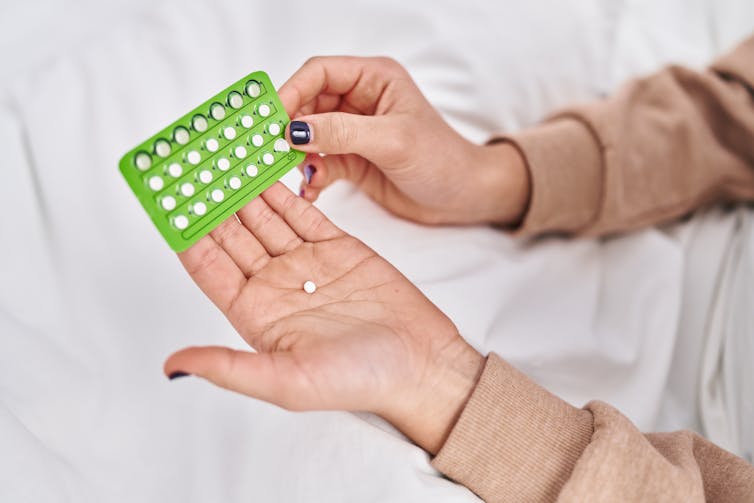 Hands holding a contraceptive pill packet.
