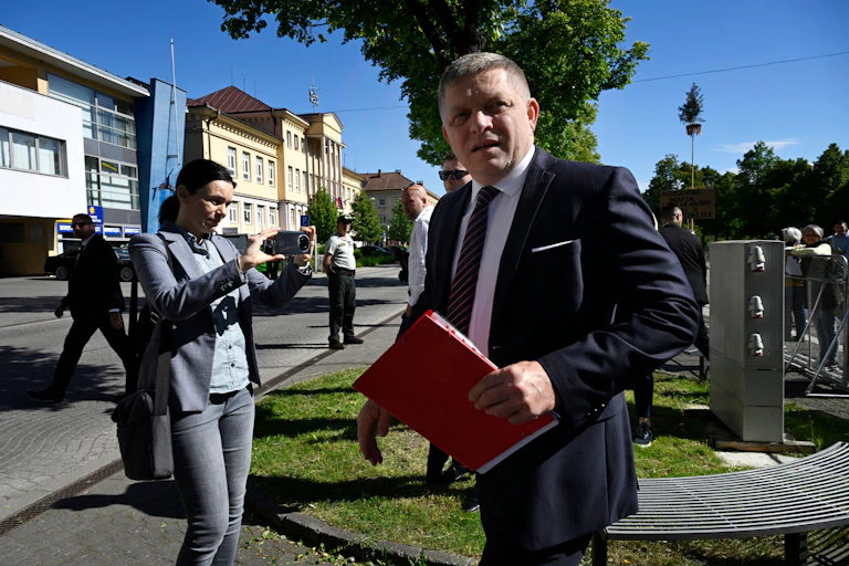 Robert Fico holding a binder of documents with security in the background.