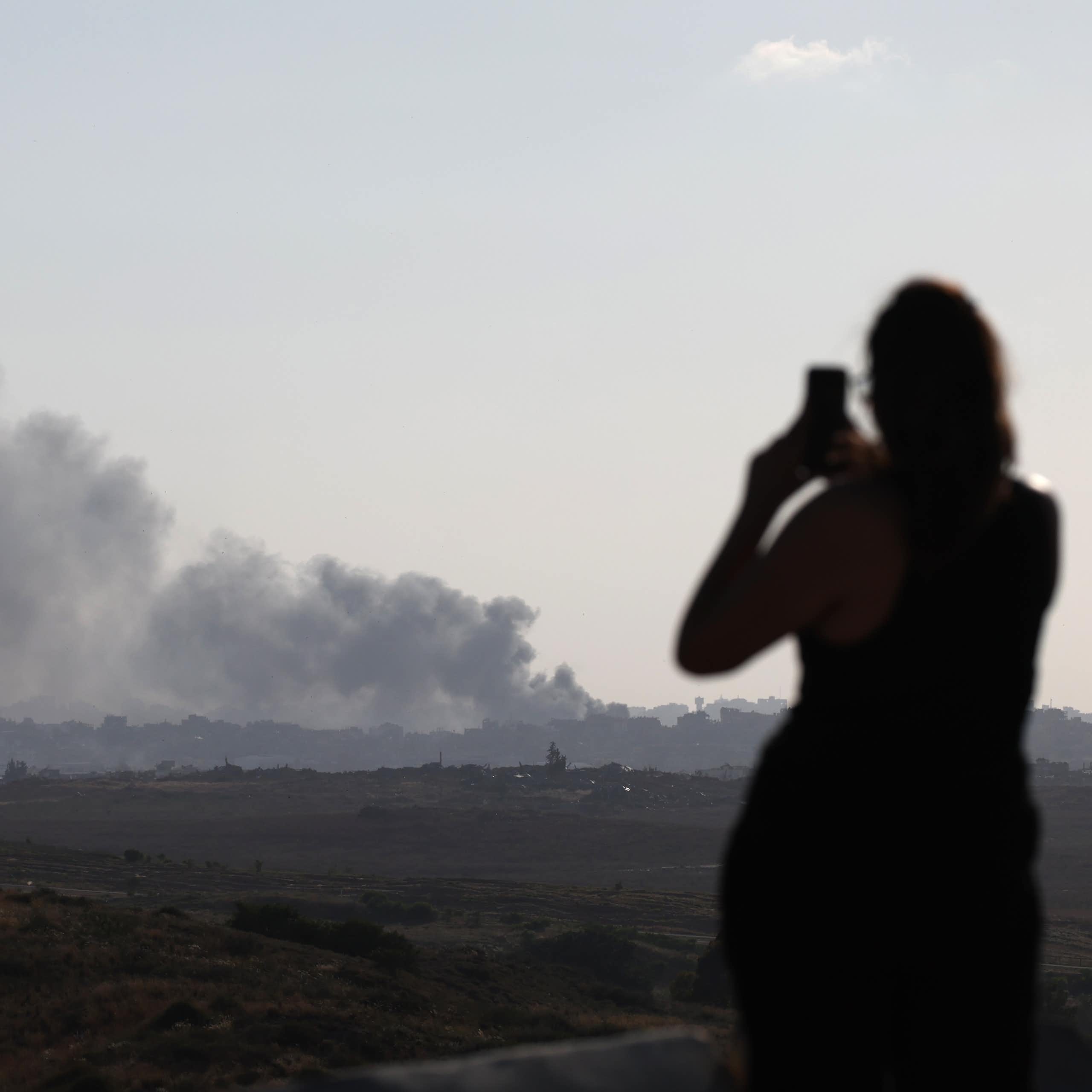 A woman looking at a large plume of smoke and filming with her phone.