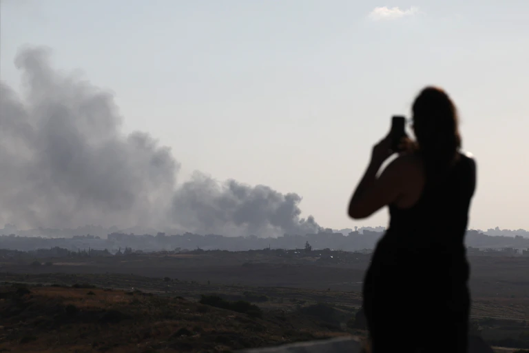 A woman looking at a large plume of smoke and filming with her phone.