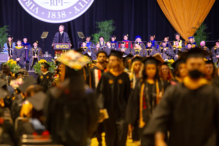 Students in caps and gowns leave while the commencement speaker is still speaking.