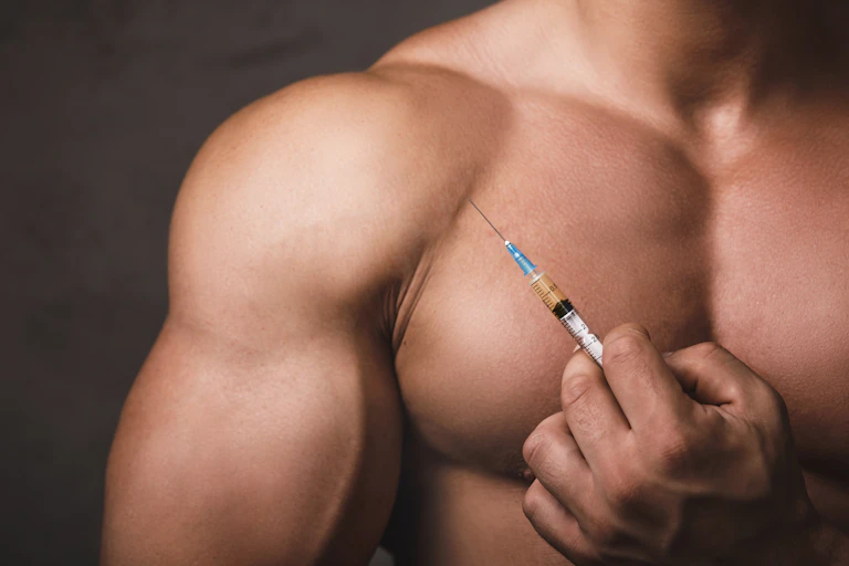A muscular man holds a medical syringe.