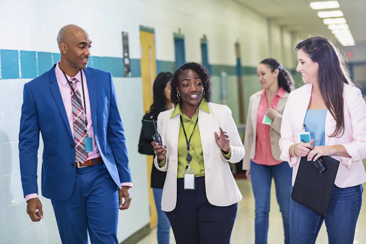 A diverse group of teachers and administrators walk down the hallway at a school.